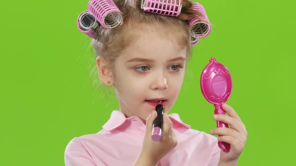 Child in Pink Curlers Looks in the Mirror and Paints with Red Lipstick Lips. Green Screen. Close Up