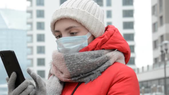 Hipster Girl in a Protective Mask with a Phone in Her Hands Writes a Message