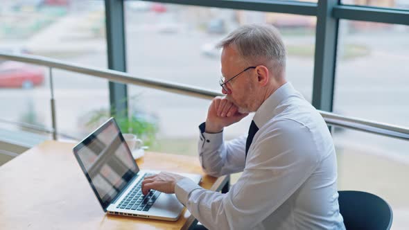 Senior businessman is working on computer in front of the window with city view