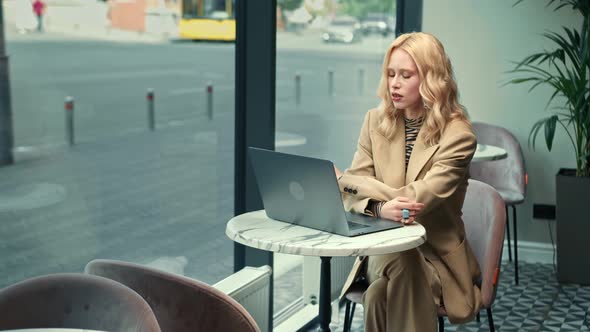 A beautiful woman works on a laptop, leads a zoom call in a cafe. Freelancer, businessman.