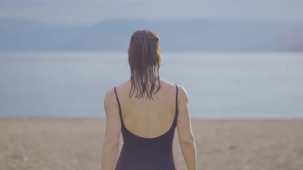 Rear view of an attractive wet girl walking on a public park beach