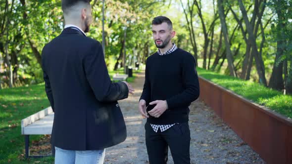 Portrait of Handsome Bearded Young Man Talking with Friend Standing in City Park on Summer Spring