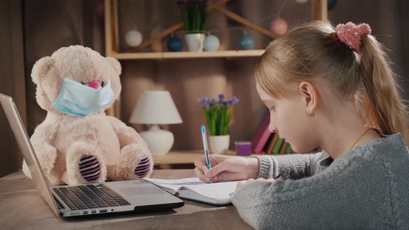 School Online  Pupil Doing Lessons Near Laptop Next to a Teddy Bear in a Protective Mask