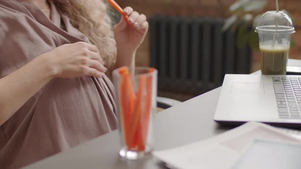 Expectant Woman Eating Carrots in Office