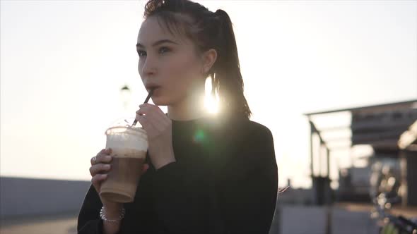 Cheerful Teenage Girl Is Sipping Cold Coffee on a Street in Evening