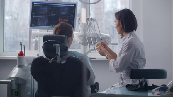 The Orthodontist Communicates with the Patient Showing Him a Cast of Teeth and an MRI Image alt