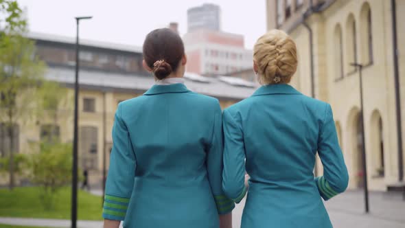 Camera Follows Two Confident Stewardesses Strolling in European City and Talking. Back View of Slim