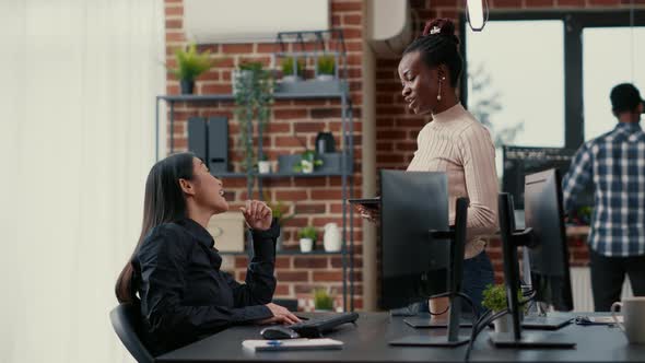 Programer Standing Up Holding Digital Tablet Talking with Coder Sitting at Desk in Front of Computer