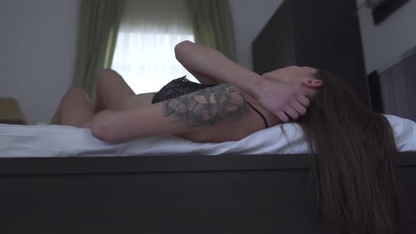 Passionate Woman with Tattoo on Shoulder Lying in the Bed Touching Her Body Close Up