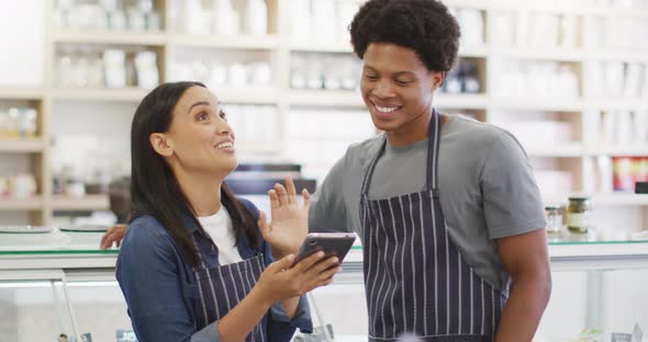 Animation of happy diverse female and male waiters using tablet at coffee shop and talking