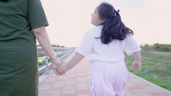 Back view of Asian mom and kid holding hand and running outdoor
