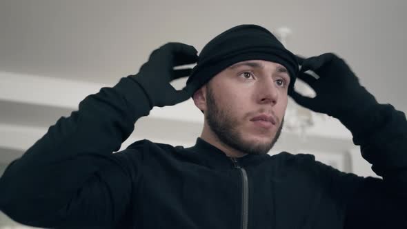 Portrait of Young Caucasian Thief in Black Clothes Putting on Balaclava Before Making Crime