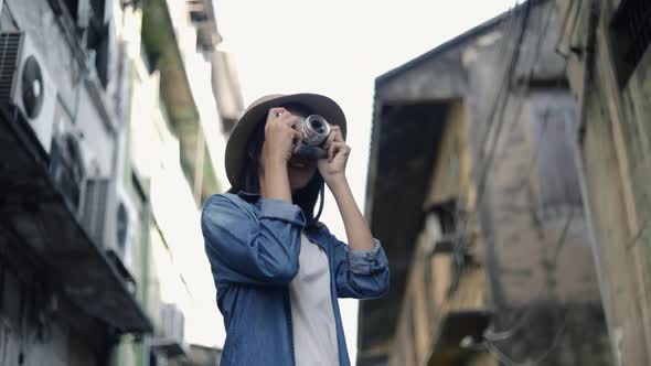 Happy Asian female traveler wearing retro fedora hat using film camera taking a photo.