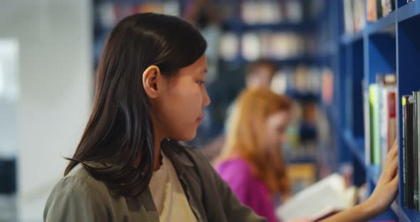 Side View of Asian Schoolgirl Searching Book on Library Shelf