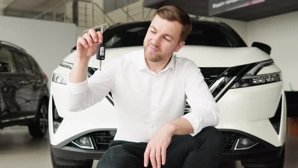 A Man with Keys Rejoices in Buying a New Car in a Car Dealership