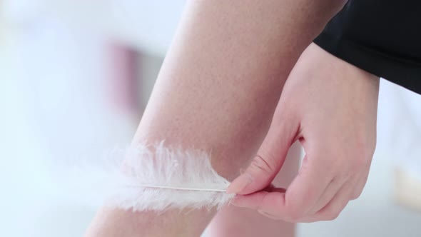 Unrecognizable Woman Runs a White Feather Across the Skin