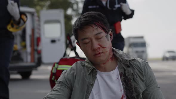 Asian Man in Blood Getting First Aid From Paramedics