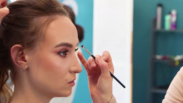 Makeup Artist Diligently Paints the Eyelid Brunette Girl in a Beauty Salon