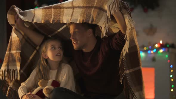 Father Telling Breathtaking X-Mas Story for Little Girl Sitting Under Cozy Plaid