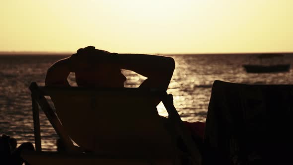 Silhouette of Man Lying on Sun Lounger Looking at the Sunset By Ocean Zanzibar