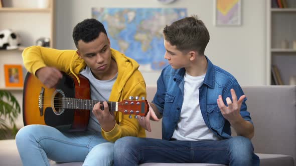 African-American Teenager Teaching Caucasian Friend to Play Guitar, Hobby