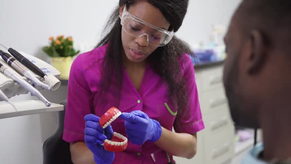 Close Up of Young Smiling African American Female Dentist Showing Teeth Model to Her Male Dark