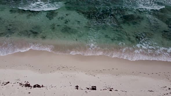 Aerial drone looking straight down over crystal clear waves crashing into an empty paradise beach in