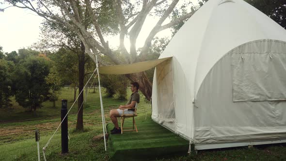 Traveler Man Enjoying Nature Sitting on Chair Near Canvas Modern Camp Tent