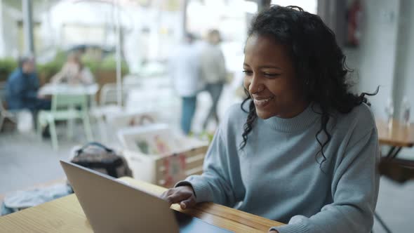 Smiling African woman wearing blue sweater talking by video call on laptop