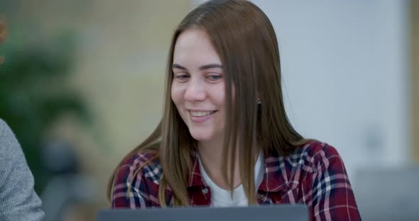 Close-up Portrait of Beautiful Young Caucasian Woman Sitting in Office with Laptop and Talking To