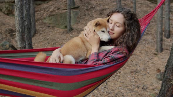 Beautiful Young Lady Hugging Cute Shiba Inu Doggy Swinging in Hammock Relaxing in Forest on Autumn