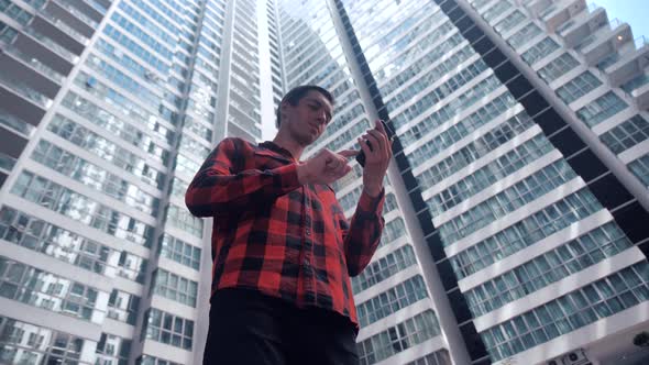 Young Man in Plaid Shirt Browsing His Smartphone in City