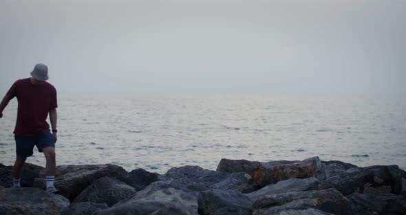 A Young Couple Walks on Large Stones Located on the Seashore Holding Hands