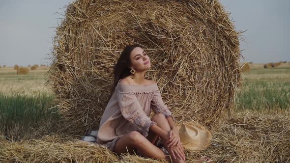 Stunning Brunette Enjoys Posing While Relaxing on the Hay in a Windy Field