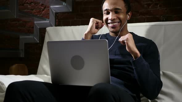 African Man Listening Music on Laptop and Dancing at Night