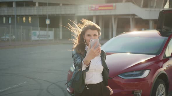 Woman Charging Electric Car and Using Smartphone is Photographed Blogs on the