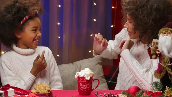 African American Mom and Little Daughter in White Sweaters Have Fun and Taste Whipped Cream with