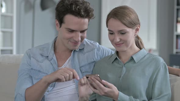 Portrait of Cheerful Couple Sitting Together and Using Smartphone