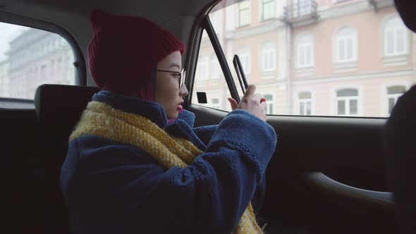 Asian Female Tourist Taking Picture and Talking via Speaker Phone in Car