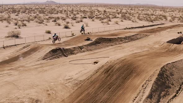 Flying over dirt race track as motocross riders race in SLOWMO, Aerial Tracking