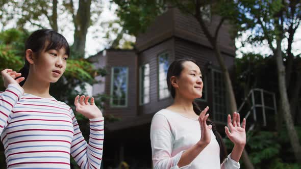 Happy asian mother exercising in garden with daughter, practicing tai chi together