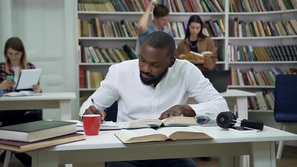 Bearded Young African Smerican Student Sitting in the Library and Working Over Home Task