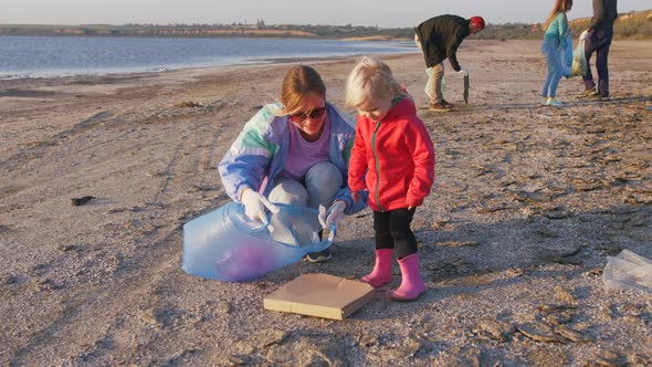 Little Girl Helps Her Parents to Clean Up Area of Dirty Beach with Garbage Bags Slow Motion