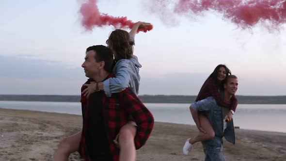 Beautiful Young Couples with Smoke Bombs in Hands on the Beach