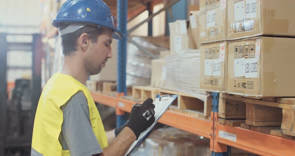 Logistics worker wearing a helmet working in a large warehouse checking inventory