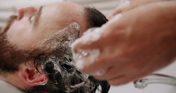 The Man in the Beauty Salon is Served Washing His Head with Shampoo and Water