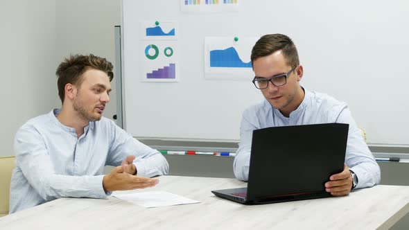 Two Office Workers Actively Discuss a Project, Come To an Agreement, Working on a Laptop.