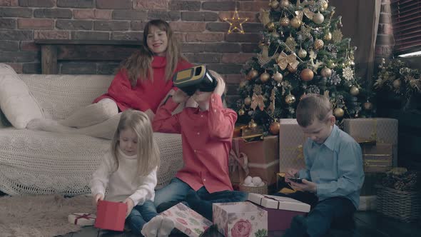 Young Woman Sits on Sofa Children Play and Open Presents