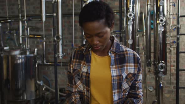 Portrait of african american woman working at gin distillery holding equipment and smiling to camera