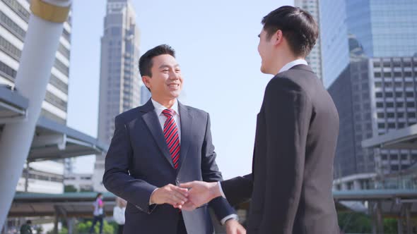 Asian businessman make handshake in city building after business deal agreement in the background.